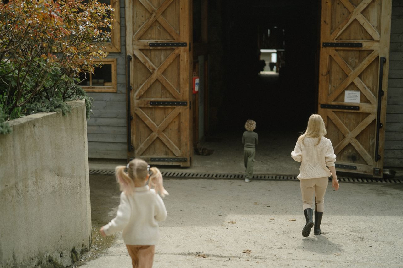 Three children walking towards a rustic wooden barn on a sunny day, exploring the outdoors.
